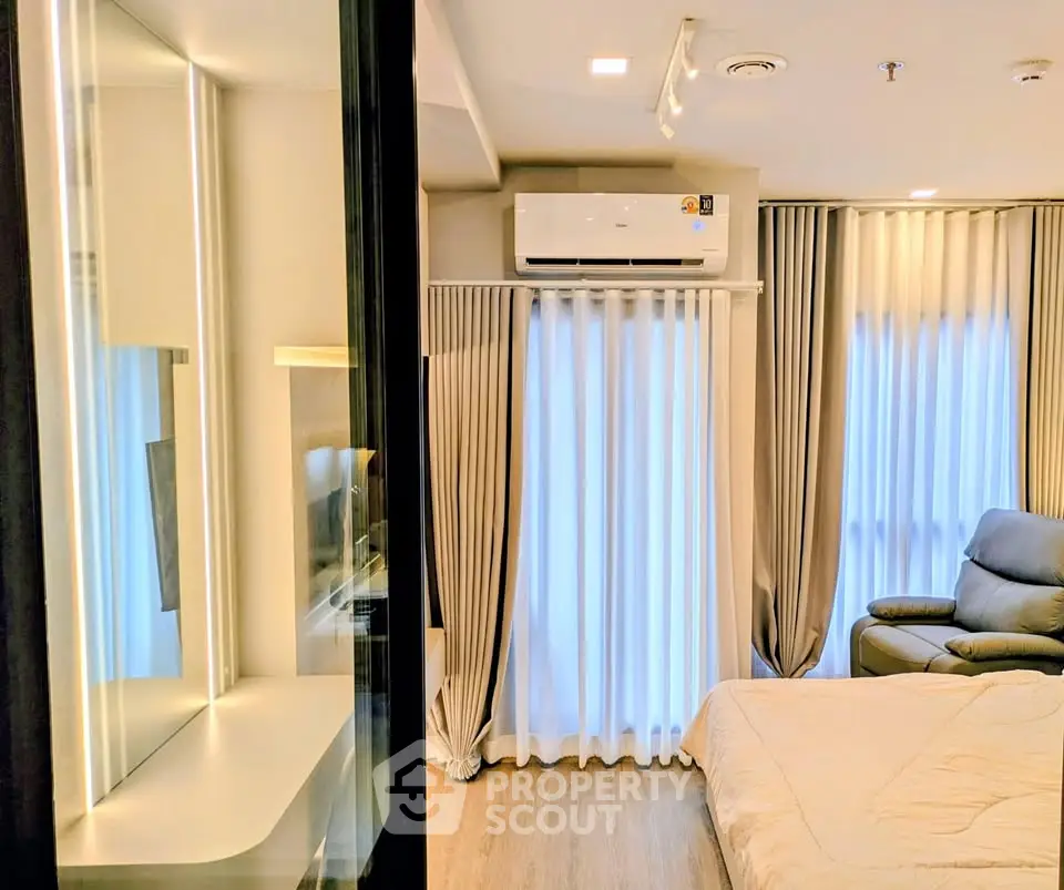 Modern bedroom with stylish decor and natural light, featuring a cozy armchair and air conditioning.