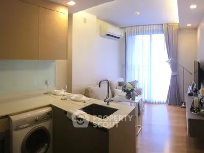 Modern open-layout living room with kitchen, featuring washing machine and cozy seating area.