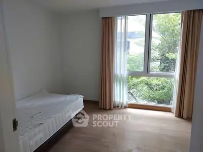 Bright bedroom with large window and garden view, featuring minimalist decor and wooden flooring.