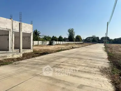 Spacious land plot with partially constructed building and paved road access.