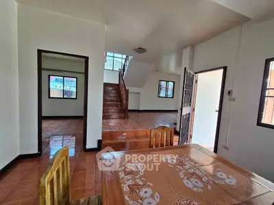 Spacious interior with tiled floors and wooden furniture, featuring a staircase and multiple windows for natural light.