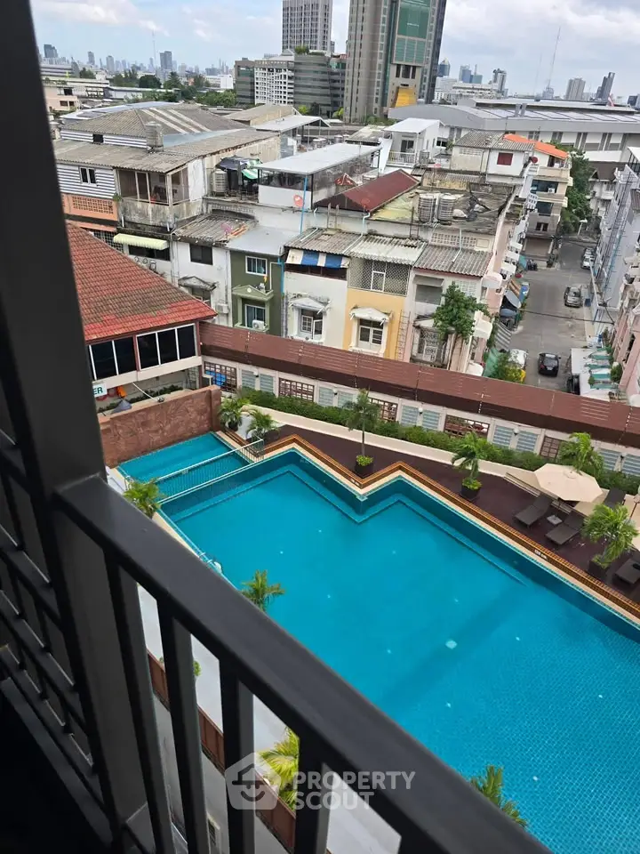 Stunning cityscape view from a balcony overlooking a luxurious swimming pool in a vibrant urban setting.