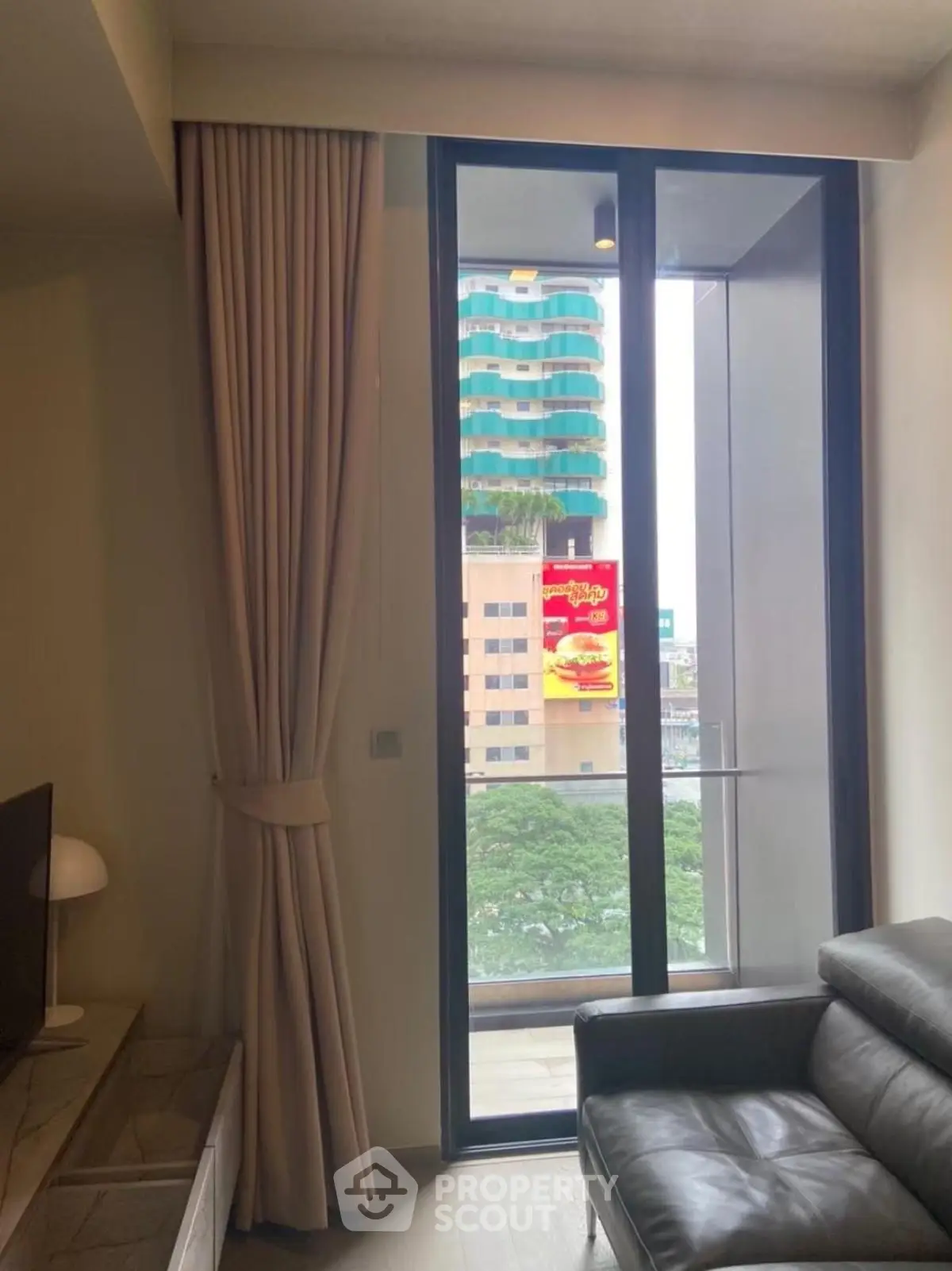 Modern living room with floor-to-ceiling window and city view, featuring a sleek leather sofa.