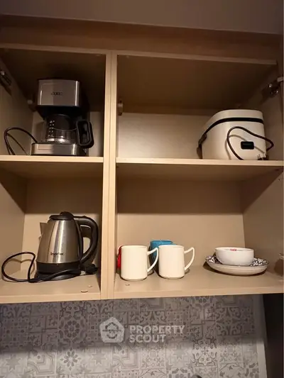 Modern kitchen cabinet with coffee maker, kettle, and cups for a cozy home setup.