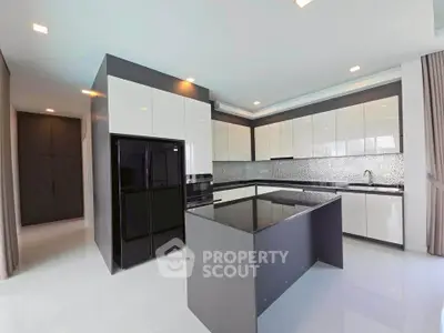 Modern kitchen with sleek cabinetry and island, featuring a glossy black refrigerator and stylish backsplash.