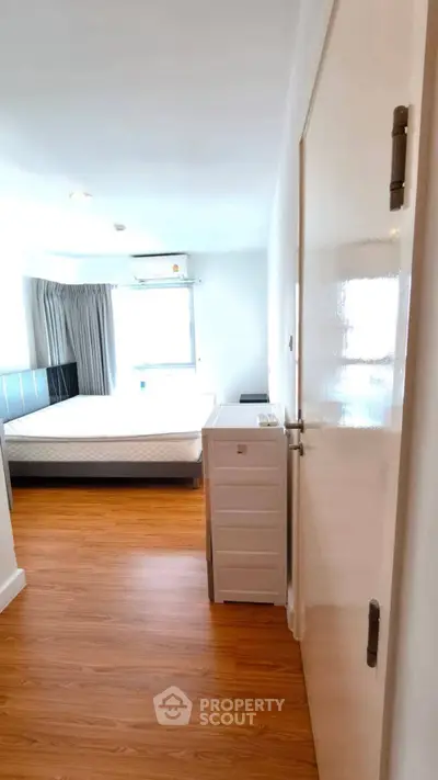 Bright bedroom with wooden flooring and large window, featuring a comfortable bed and modern decor.