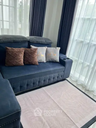 Elegant living room with plush blue sofa and large windows with sheer curtains.