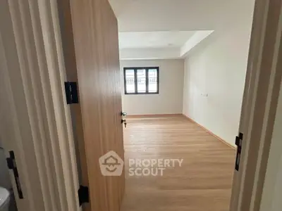 Spacious empty room with wooden flooring and large window, perfect for customization.