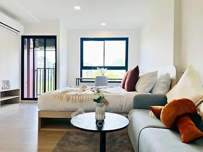 Modern studio apartment with cozy bed and stylish decor, featuring large windows and natural light.