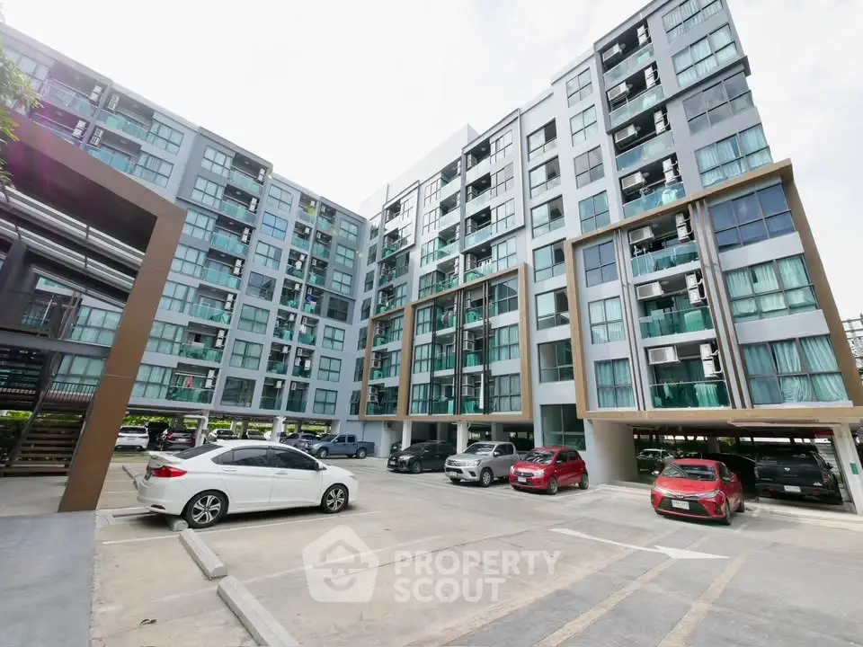 Modern apartment building with parking area and multiple cars in front, showcasing urban living.