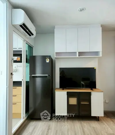 Modern living room with sleek fridge and TV setup, featuring stylish cabinetry and air conditioning.