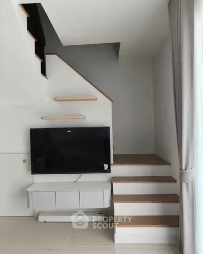 Modern living room with stylish staircase and mounted TV, perfect for contemporary living.