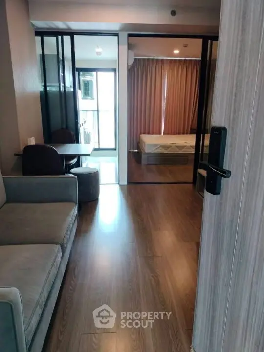 Modern apartment interior with cozy living room and bedroom, featuring sleek wooden flooring and glass partitions.
