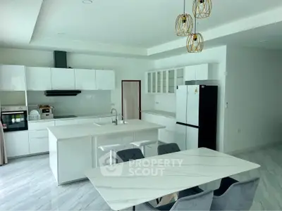 Modern kitchen with sleek white cabinetry, island, and dining area in a contemporary home.