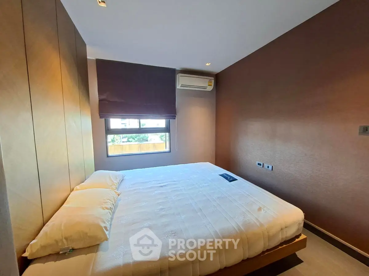 Modern bedroom with large window and air conditioning unit, featuring a cozy bed and stylish decor.