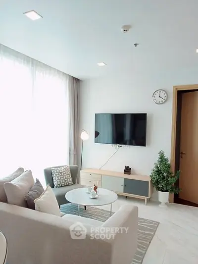 Modern living room with stylish furniture and wall-mounted TV, featuring natural light and minimalist decor.