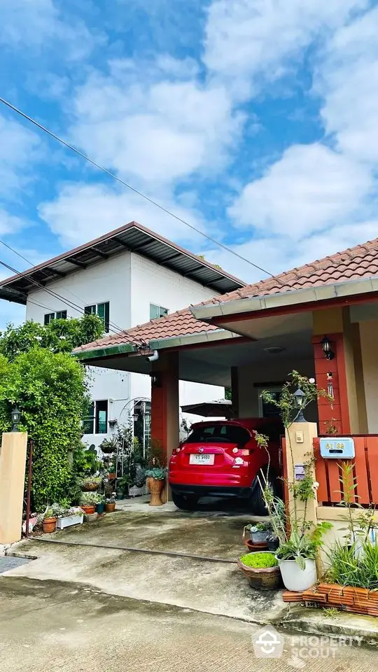 Charming two-story home with a covered carport and vibrant garden, showcasing a spacious driveway and a welcoming entrance under a clear blue sky.