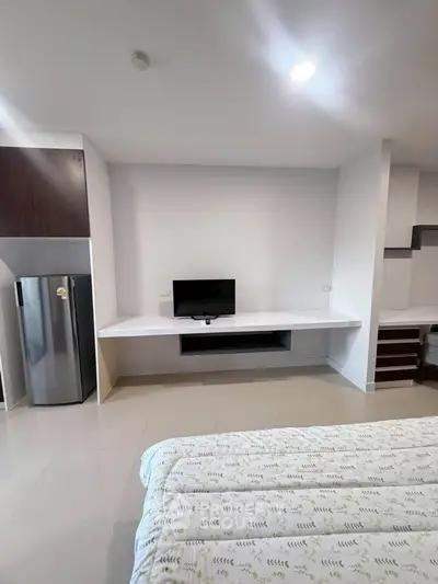 Modern bedroom with sleek TV setup and stainless steel fridge, perfect for urban living.