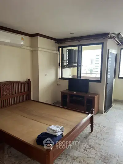 Spacious bedroom with wooden bed frame and large windows offering city views