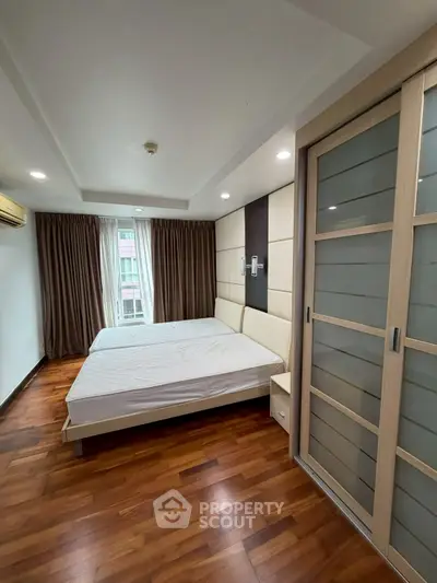 Spacious bedroom with wooden flooring and sliding closet doors in modern apartment.