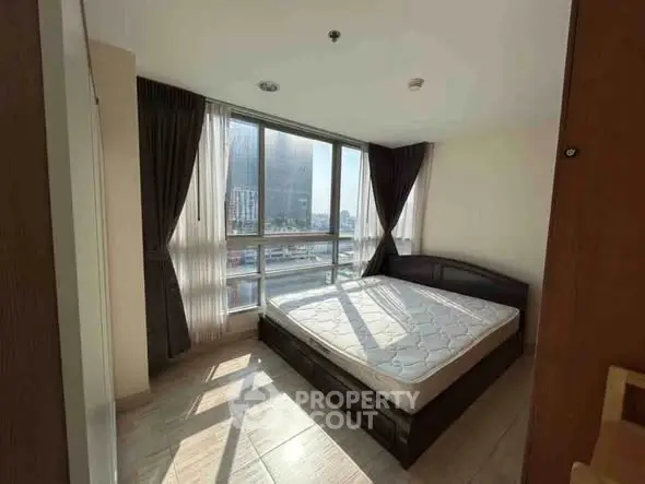 Bright bedroom with large windows and city view, featuring a comfortable bed and modern decor.