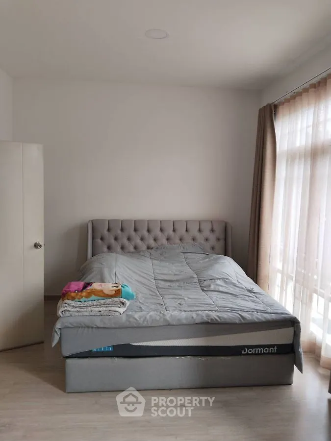 Cozy bedroom with plush bed and natural light through large windows.