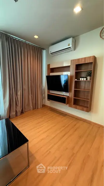 Modern living room with wooden flooring, wall-mounted TV, and air conditioning unit.