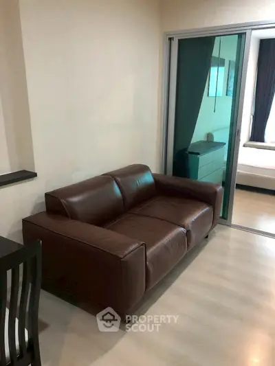 Modern apartment interior with brown leather sofa and sliding glass door to bedroom.