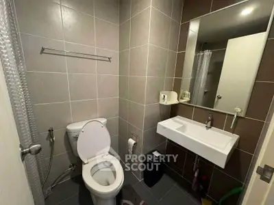 Modern bathroom with sleek fixtures and neutral tiles, featuring a toilet, sink, and mirror.