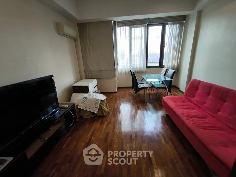 Cozy living room with wooden flooring, red sofa, and dining area by large window.