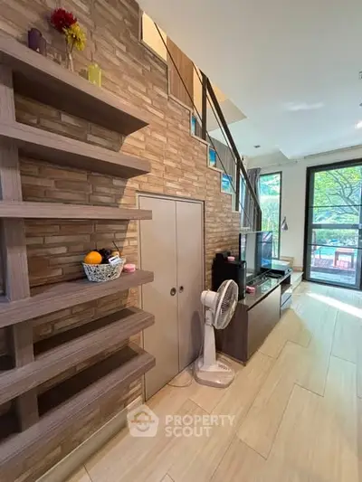 Modern living room with stylish brick wall, wooden shelves, and large windows offering natural light and garden view.