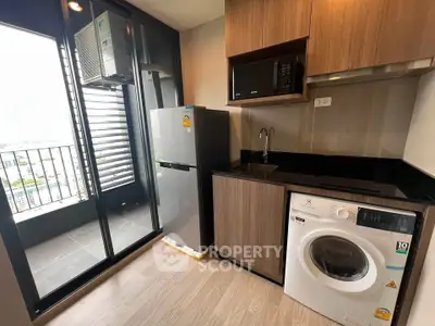 Modern kitchen with balcony, featuring fridge, microwave, and washing machine in sleek design.