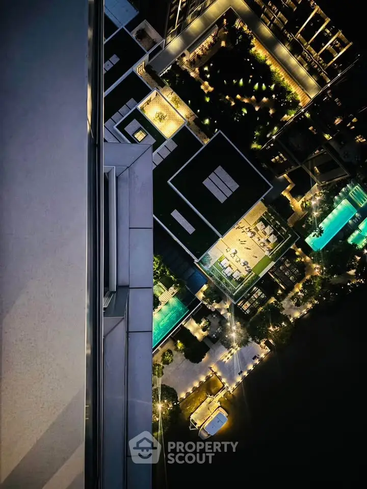 Stunning aerial view of modern residential complex with illuminated pools and gardens at night.