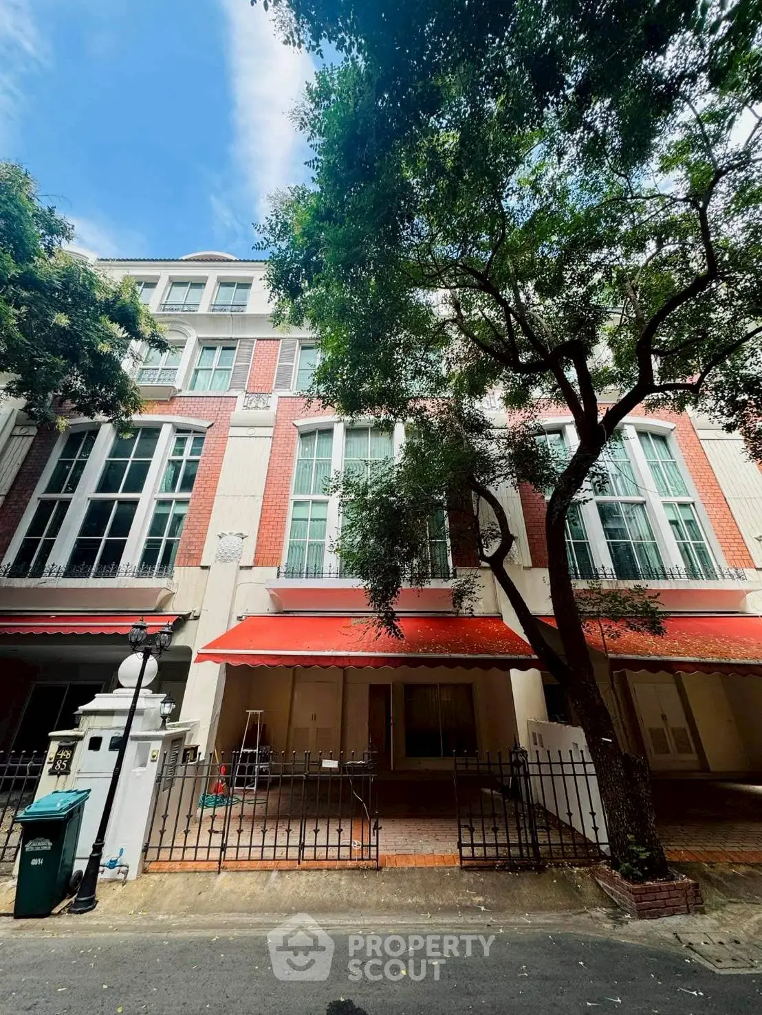 Charming townhouse with red awnings and lush trees in a serene neighborhood.
