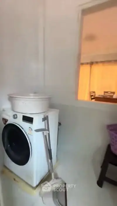Compact laundry area with washing machine and window view into dining space.