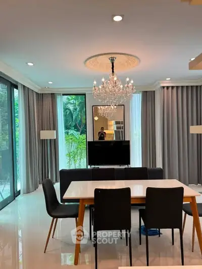 Elegant dining area with chandelier and garden view, featuring modern furniture and floor-to-ceiling windows.