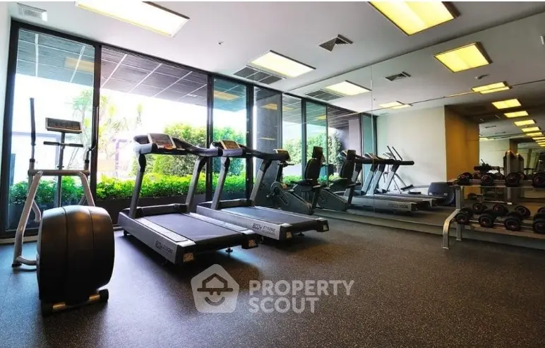 Modern gym with treadmills and weights, large windows with garden view, ideal for fitness enthusiasts.