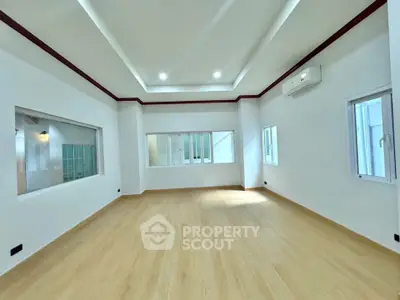 Spacious modern room with wooden flooring and multiple windows for natural light.