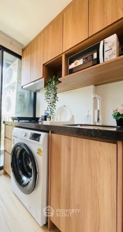 Modern laundry area with wooden cabinets and washing machine in bright apartment.