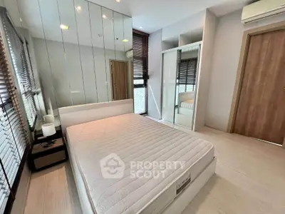 Modern bedroom with mirrored wall, sleek furniture, and natural light.