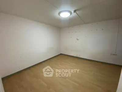 Spacious empty room with wooden flooring and ceiling light, ideal for customization.