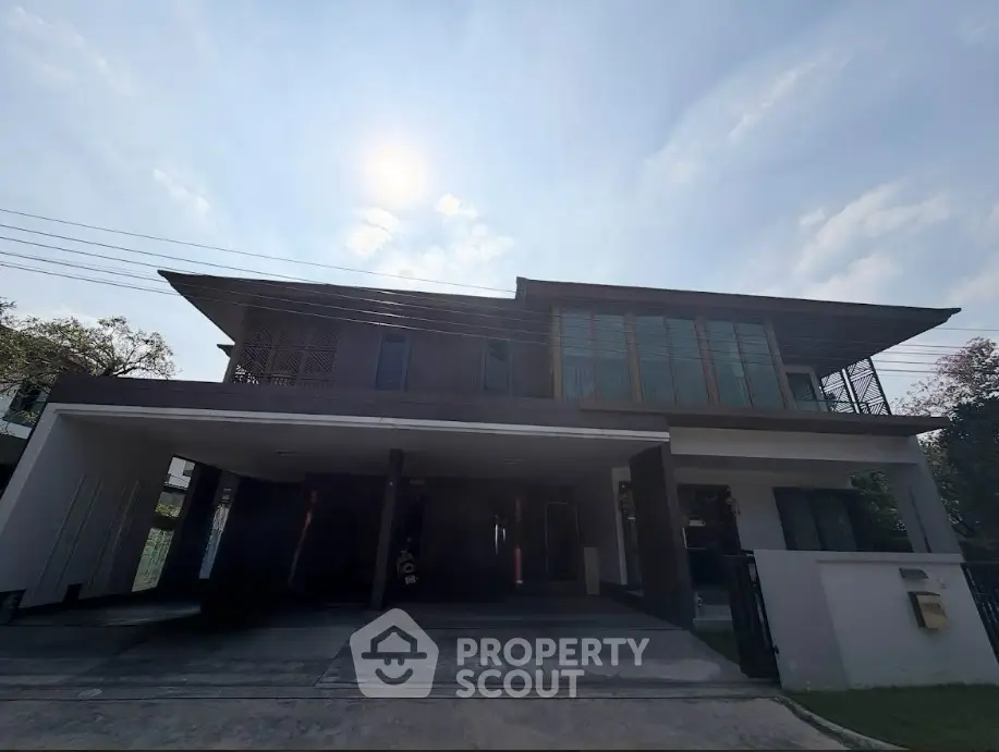 Modern two-story house with large windows and covered parking area.