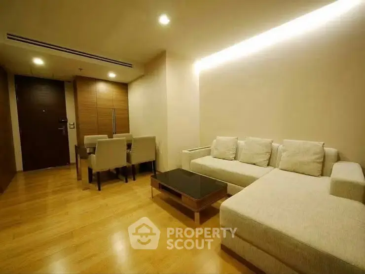 Modern living room with cozy sectional sofa and elegant dining area, featuring warm wooden flooring and ambient lighting.