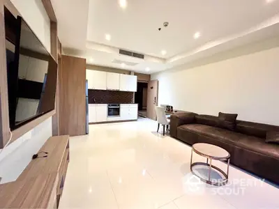 Modern living room with open kitchen, sleek furniture, and bright lighting.