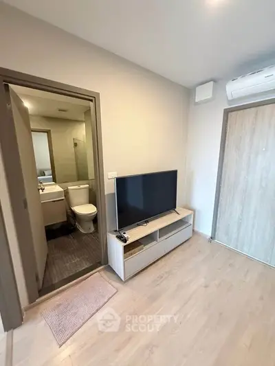 Modern apartment interior with TV and bathroom view, featuring sleek design and air conditioning.