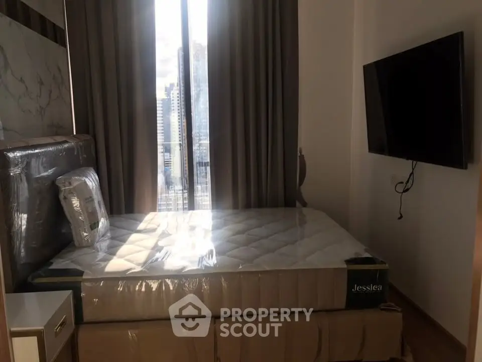Modern bedroom with large window and wall-mounted TV in a high-rise apartment.