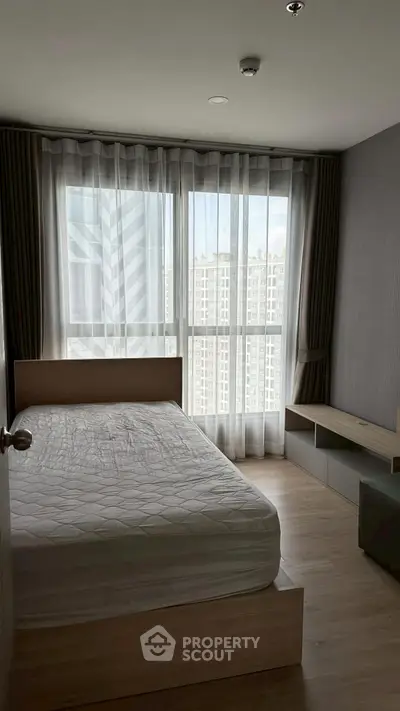 Modern bedroom with large window and city view, featuring a minimalist design and natural light.