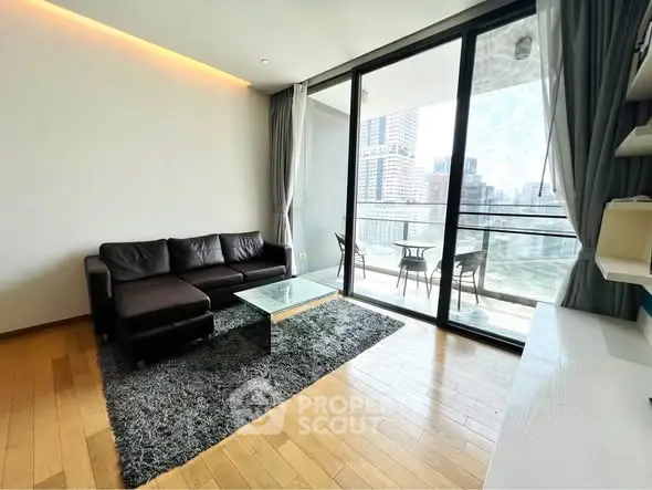 Modern living room with large glass doors leading to a balcony with city views, featuring a sleek black sofa and stylish decor.