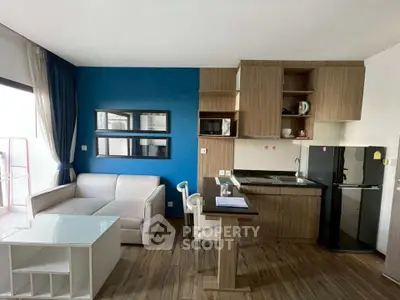 Modern studio apartment with stylish kitchen and cozy living area, featuring sleek wooden flooring and vibrant blue accent wall.