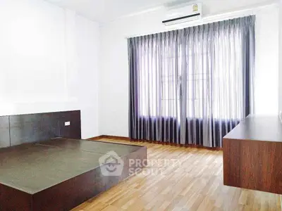 Spacious bedroom with wooden flooring and large window with curtains, featuring a modern bed frame.